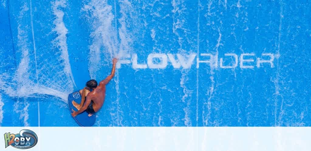 An aerial view of a person wakeboarding on a water surface with the words flow rider written in the water.