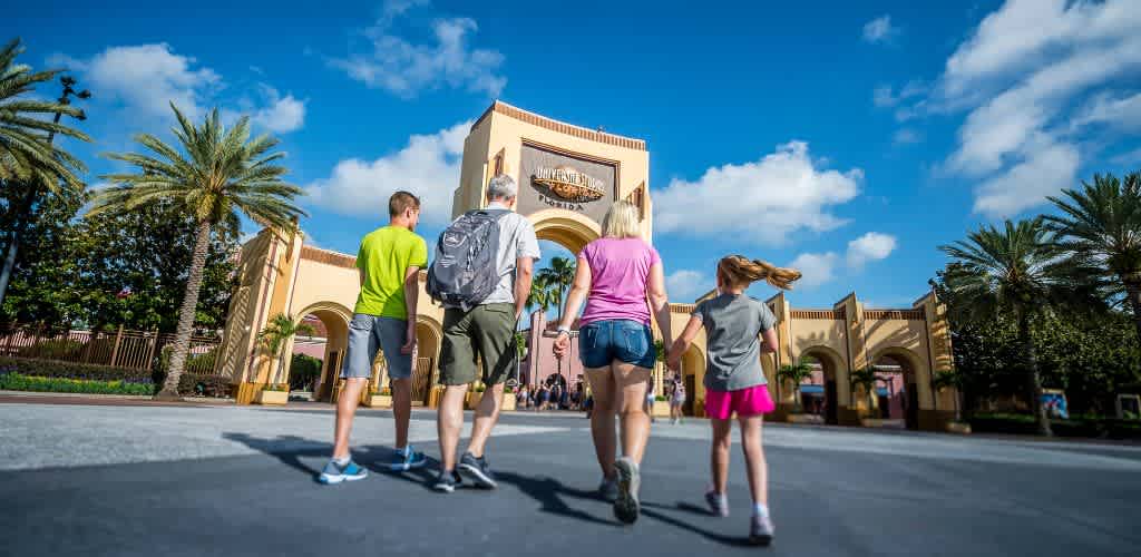 A family walking toward the entrance of Universal Orlando Resort on a sunny day with palm trees and a blue sky.