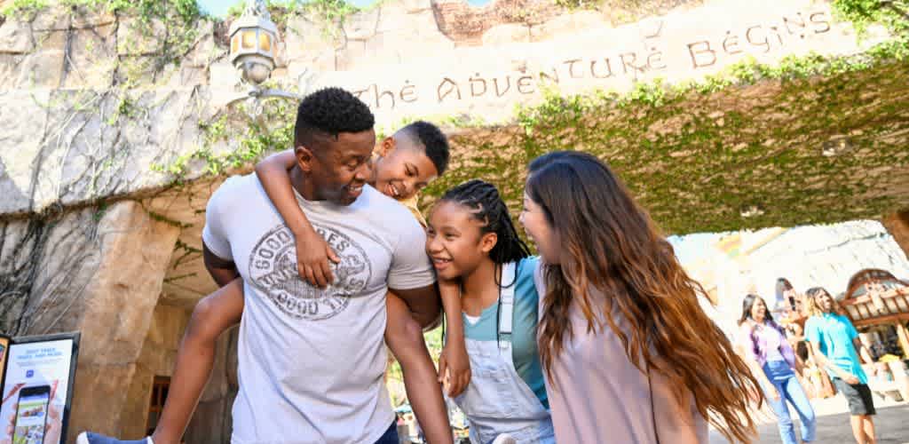 A happy family enjoying time together outdoors at an amusement park with greenery and scenic background.