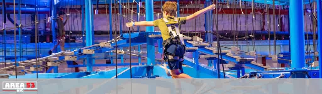 Child in harness walking across a high ropes course at Funex Adventure Park with colorful equipment and safety features