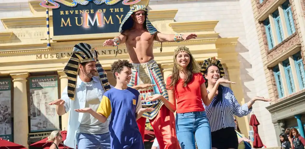 Group of people in Egyptian costumes performing a dance outside a museum with a large Revenge of the Mummy sign above.