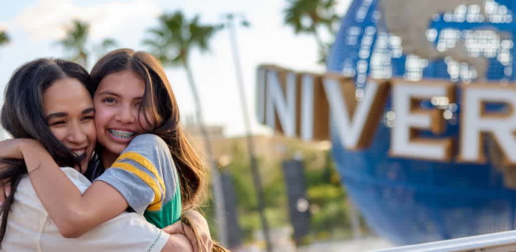 Two smiling girls hugging in front of the Universal Studios globe at an amusement park