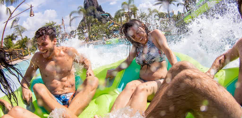 People enjoying a water ride on a green inflatable raft at a water park on a sunny day.
