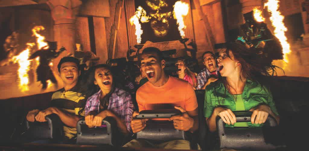 Group of excited people riding a roller coaster with fire effects in the background at an amusement park