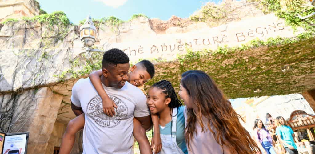 Four people smiling and laughing together outdoors at a theme park called Adventure Begins with rocky structures and greenery in the background.