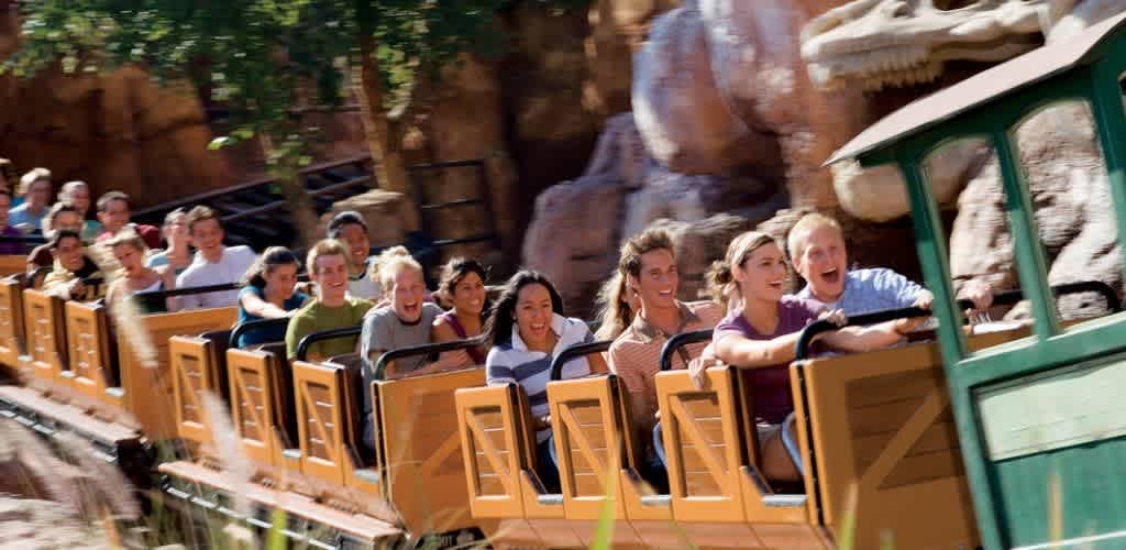 Agroup of smiling people enjoying a roller coaster ride outdoors on a sunny day with rocky scenery in the background