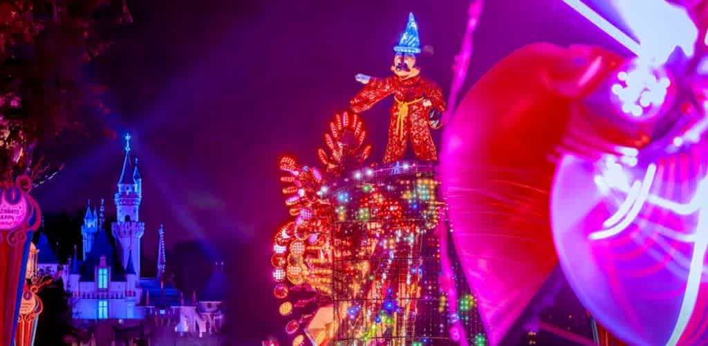 Colorful amusement park ride with a large Mickey Mouse figure wearing a wizard hat illuminated by bright neon lights