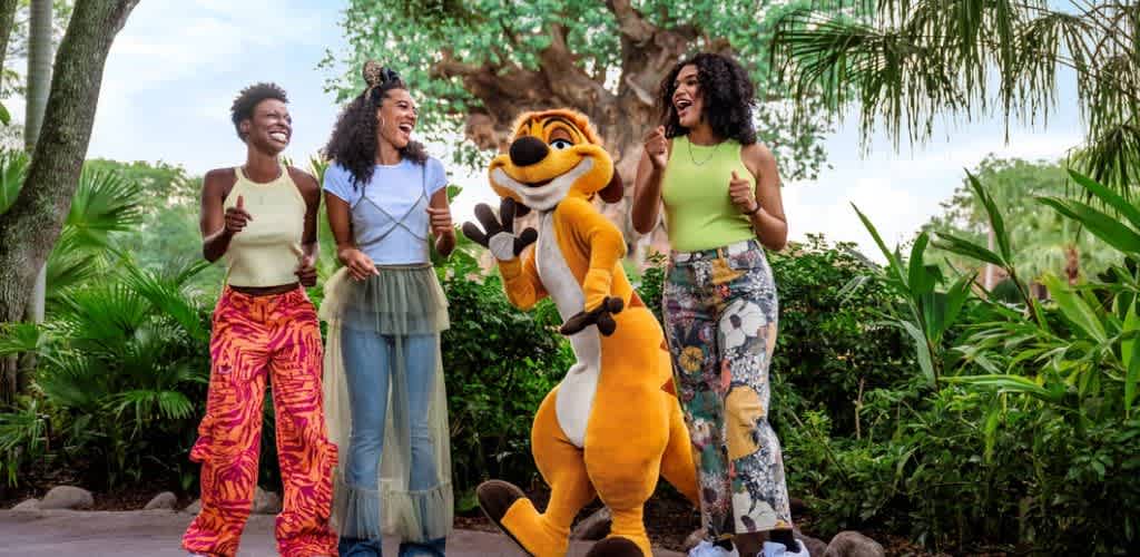 Three women stand outdoors with a costumed character of a cheerful cartoon animal among lush green trees and plants