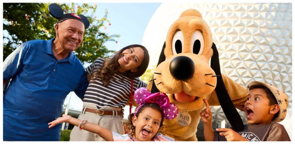 A happy family with two children and a woman pose with a person dressed as Pluto the dog outdoors during daytime.