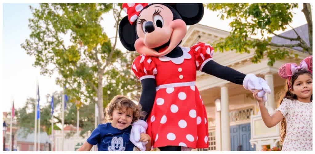Two children holding hands with Minnie Mouse character at a theme park outdoor setting