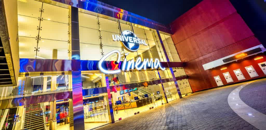 Exterior view of Universal Cinema with bright lights, a large illuminated sign, and a curved pathway leading to ticketing and entrance areas