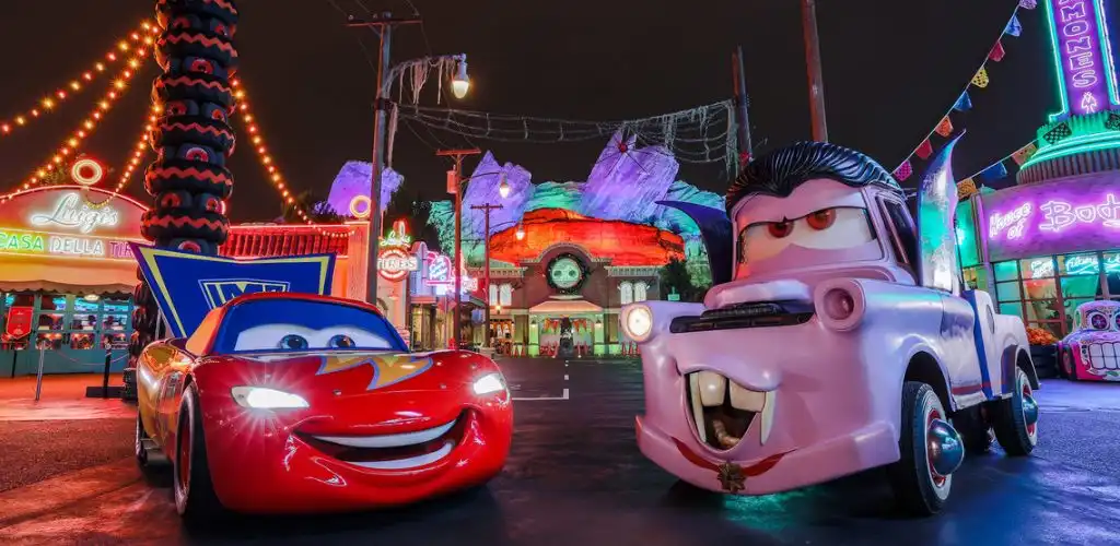 Colorful animated cars with smiling faces and sunglasses at a lively amusement park nighttime scene with bright lights and themed attractions.