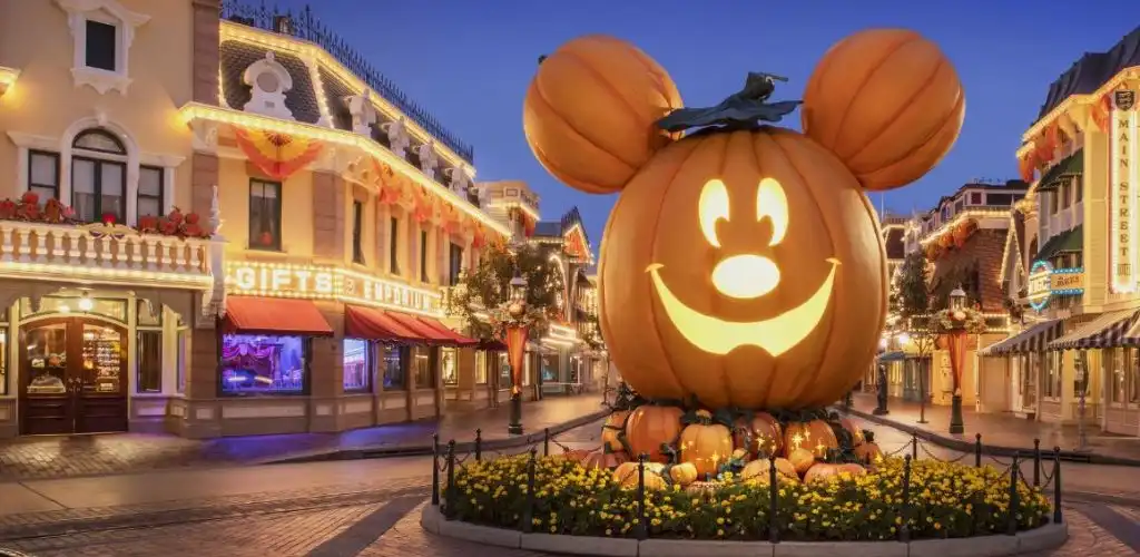 Large illuminated jack-o'-lantern featuring Mickey Mouse's face with ears, pumpkin top hat, surrounded by smaller pumpkins in a festive street scene at dusk
