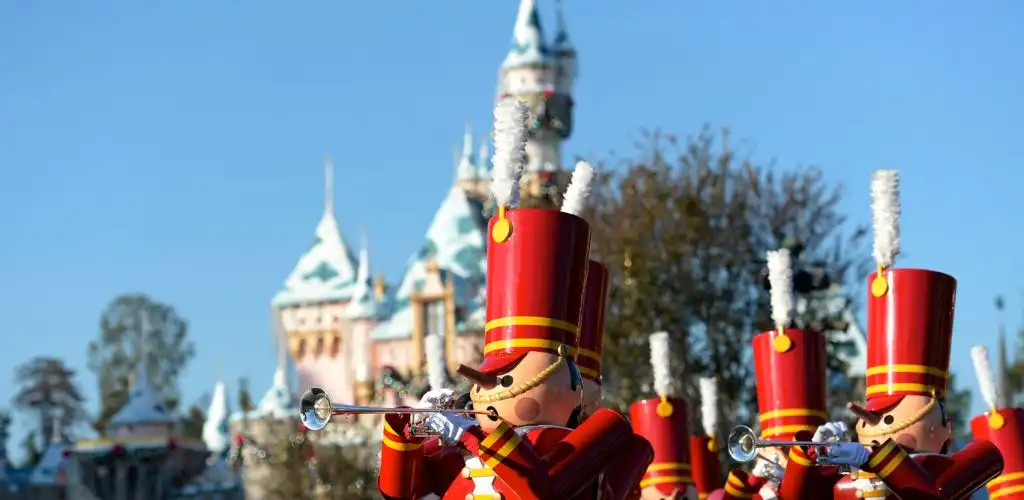 Toy marching soldiers in bright red uniforms with tall hats parade in front of a castle against a clear blue sky
