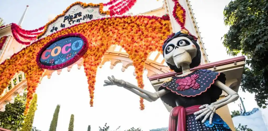 Three people with dark silhouettes watching a colorful holiday light display featuring various shapes and buildings at night