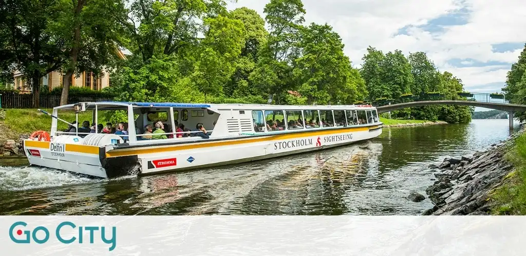 A sightseeing boat with passengers traveling along a river surrounded by green trees during daytime.