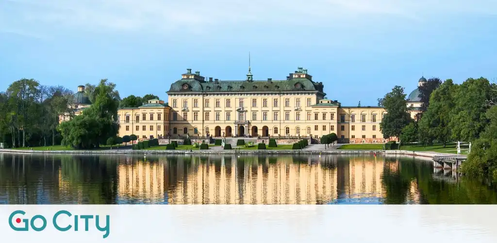 Luxury palace with a pond reflecting its image, surrounded by trees and greenery, under a clear blue sky