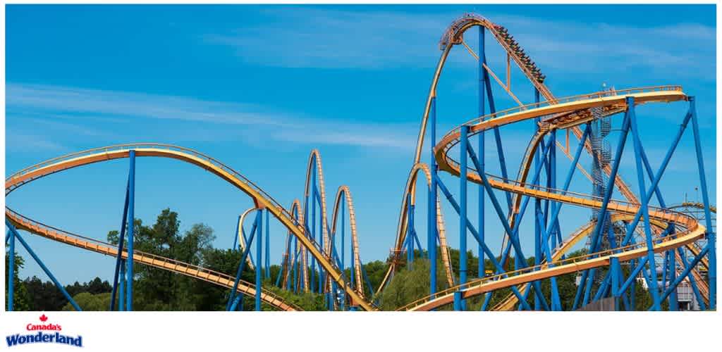 A colorful roller coaster with yellow tracks and blue supports against a blue sky and green trees in the background