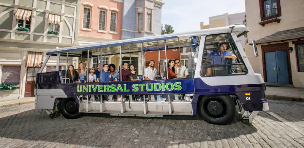 A group of people enjoying a guided tour on a trolley with Universal Studios signage, set on a cobblestone street in front of colorful buildings.