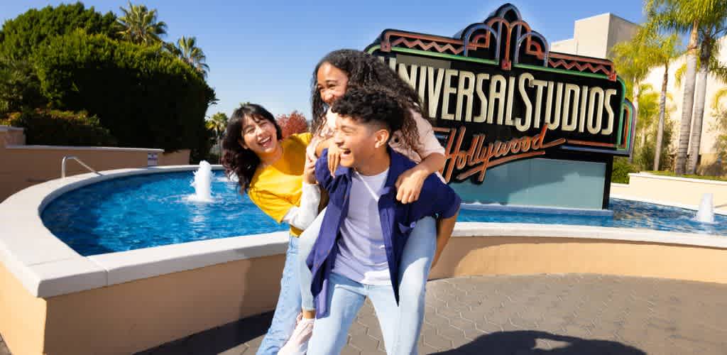 Three smiling people stand in front of universal studios hollywood sign at theme park during daytime