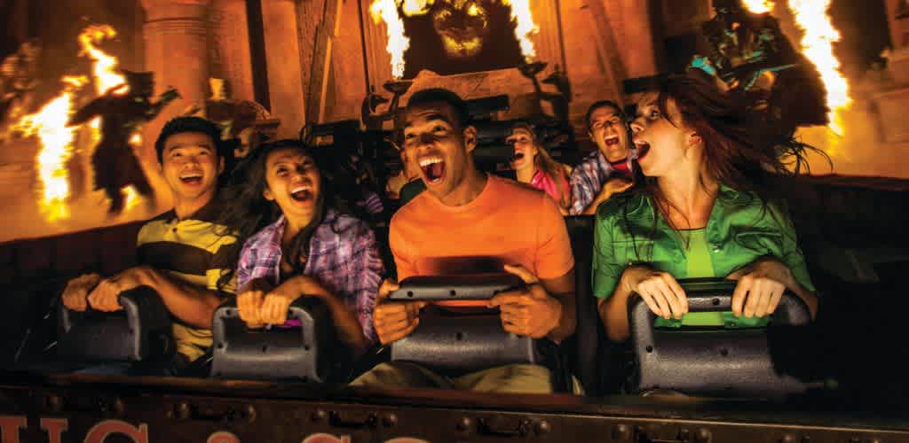 Group of diverse people enjoying a thrilling amusement park ride with fire effects and bright smiles in a dark indoor setting