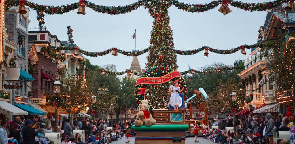 A festive Christmas scene at a theme park with a decorated tree, holiday lights, costumed characters, and visitors celebrating during the day