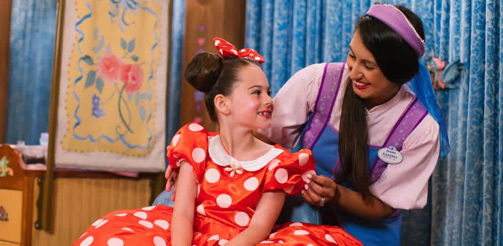 A woman dressed as Snow White comforts a girl wearing a red polka dot dress and bow in her hair in a colorful themed setting.