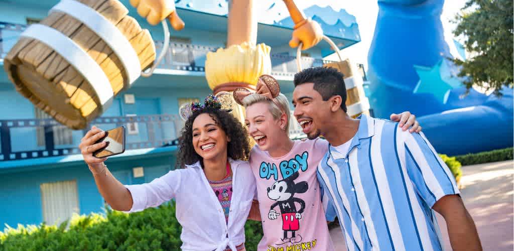 Three friends smiling and taking a selfie at a colorful amusement park with water slides in the background