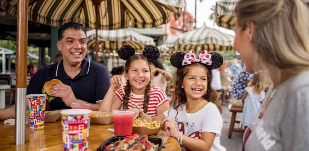 A family enjoying meals outdoors at a lively restaurant with striped umbrellas and colorful drink cups.