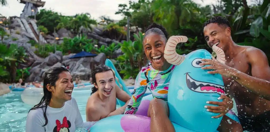 Four smiling people enjoying a pool with a colorful inflatable dragon outdoors on a sunny day.