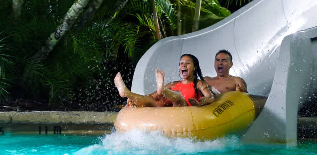 Two children are enjoying a ride on a 
                                  yellow water slide into a pool at a water park.