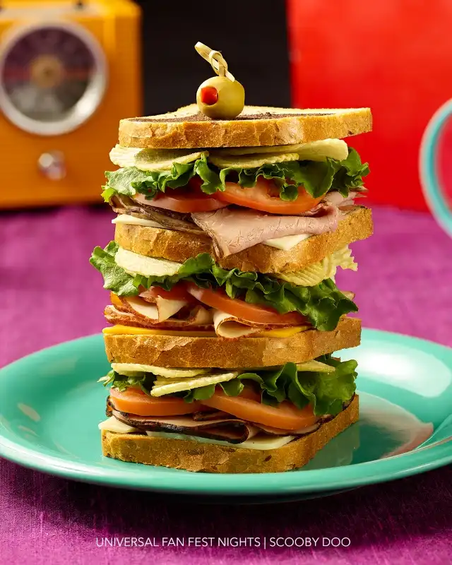 A tall stack of multiple sandwich slices with lettuce, tomato, and various deli meats on a turquoise plate.
