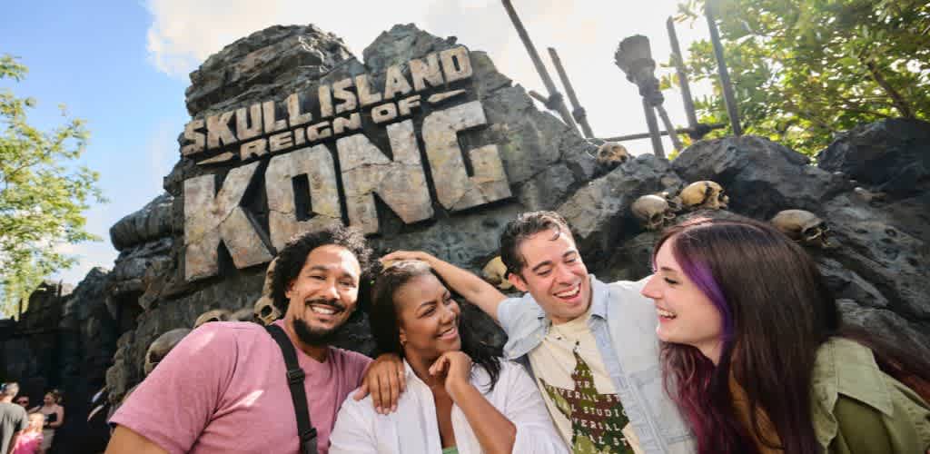 Four people smiling and enjoying themselves in front of a Skull Island Reign of Kong sign at an amusement park.