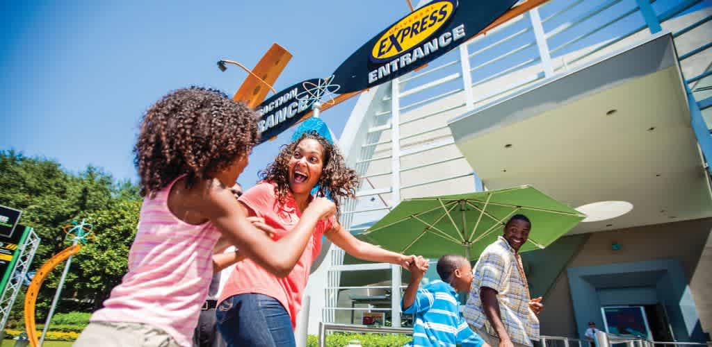 Four smiling people enjoy outdoors at front of funex amusement park entrance on sunny day with clear blue sky