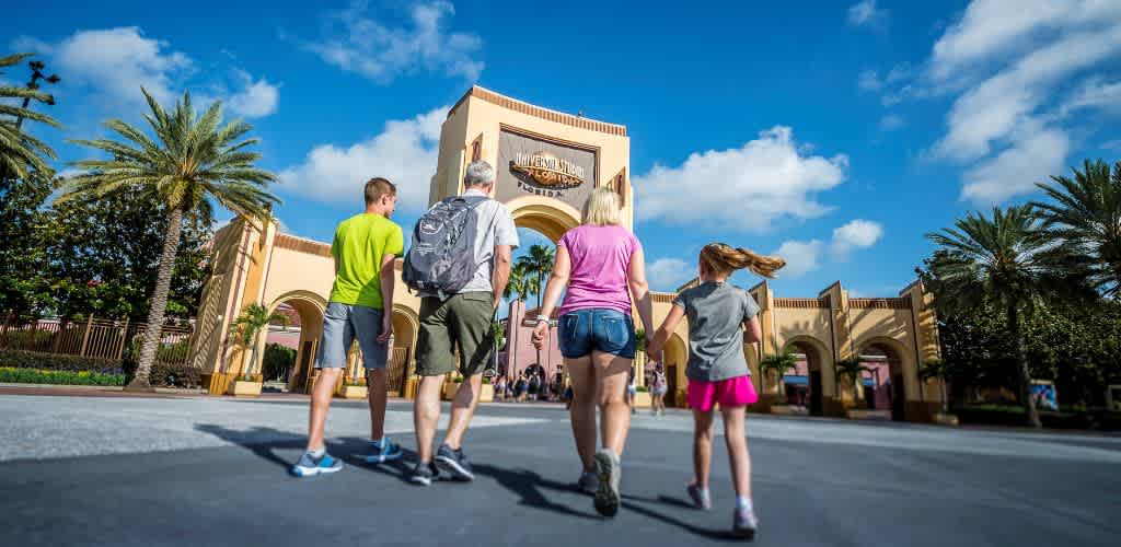 Family walking towards Universal Studios Florida entrance on a sunny day with palm trees and blue sky in the background