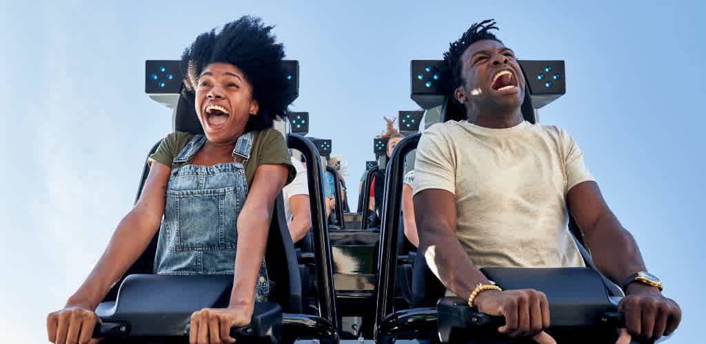 Two excited people on a roller coaster ride with their hands in the air and wide smiles, enjoying the thrill and fun of the amusement park.