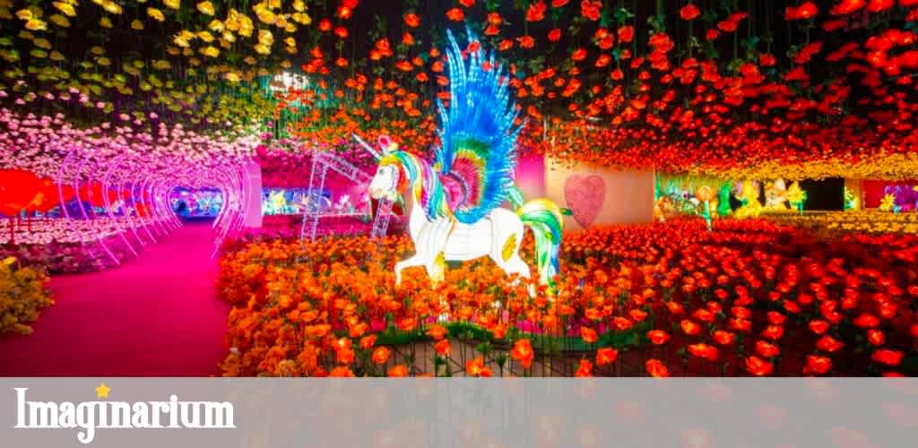 A colorful garden display with a rainbow maned unicorn sculpture surrounded by vibrant flowers and illuminated decorations.