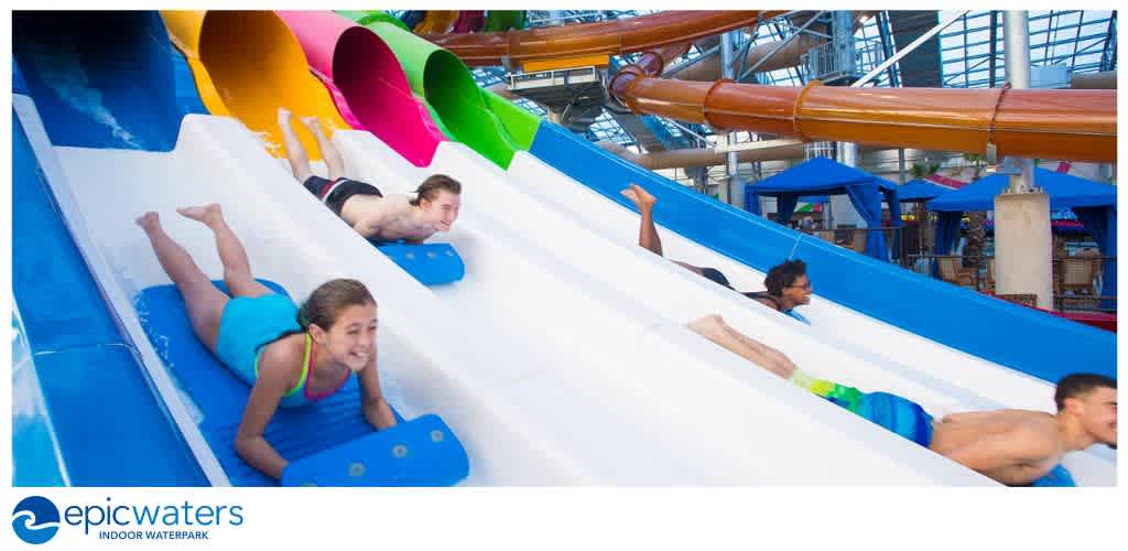 Children and teenagers enjoying a water slide at an indoor waterpark with colorful slides and a glass ceiling