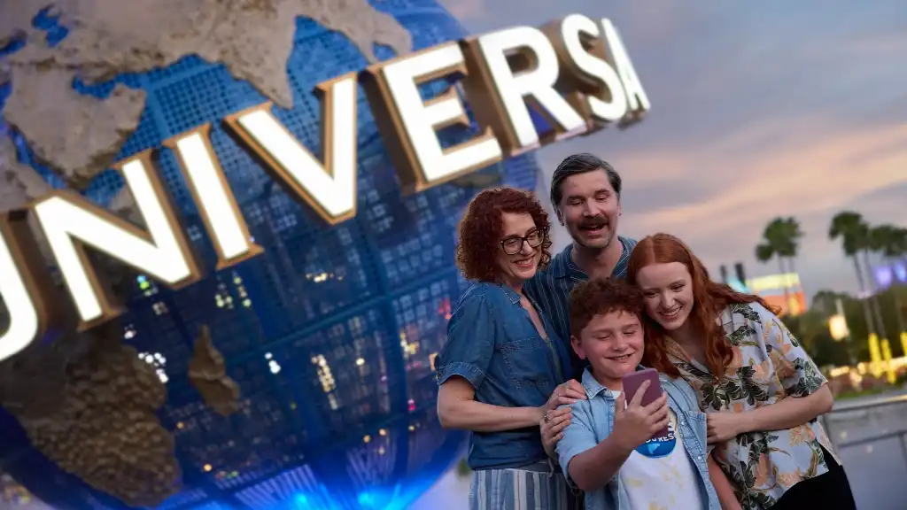 A smiling family of four, two adults and two children, standing together outside near a Universal Studios sign at sunset.