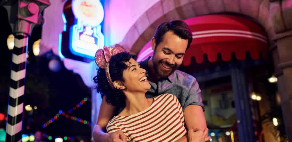 A smiling couple sharing a joyful moment outdoors at night with colorful lights and a festive atmosphere.