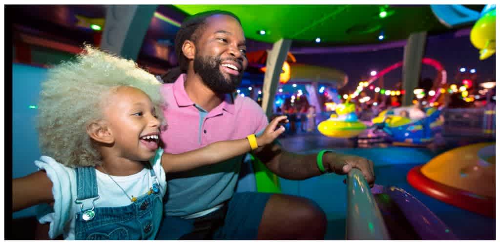 A joyful man and girl enjoying a colorful amusement park ride at night with bright lights and spinning attractions.