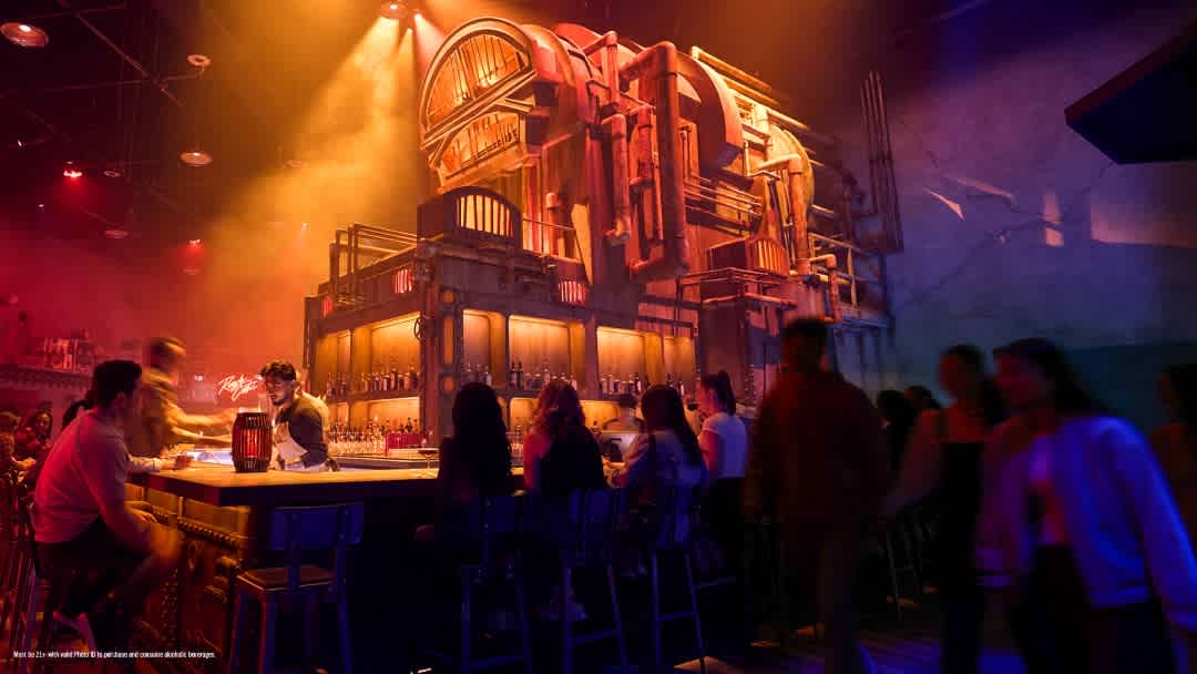 A lively bar with colorful lighting, a central bar counter, and people socializing in a vibrant entertainment venue with an industrial style setting.