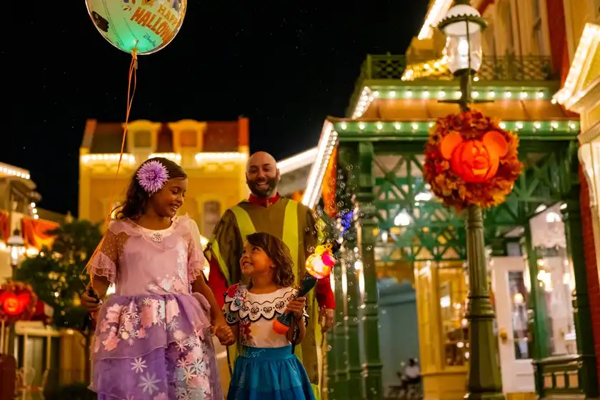 A woman in a plaid shirt hands out candy to children in costumes during a festive Halloween event at night