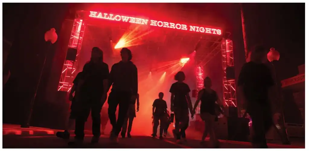 People walking towards a Halloween Horror Nights stage with bright red lighting and silhouettes of attendees in front