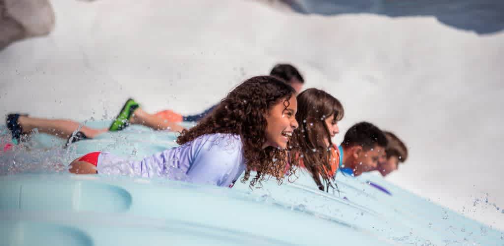 Group of children smiling and lying on a surfboard in the water at a fun outdoor activity in bright sunlight