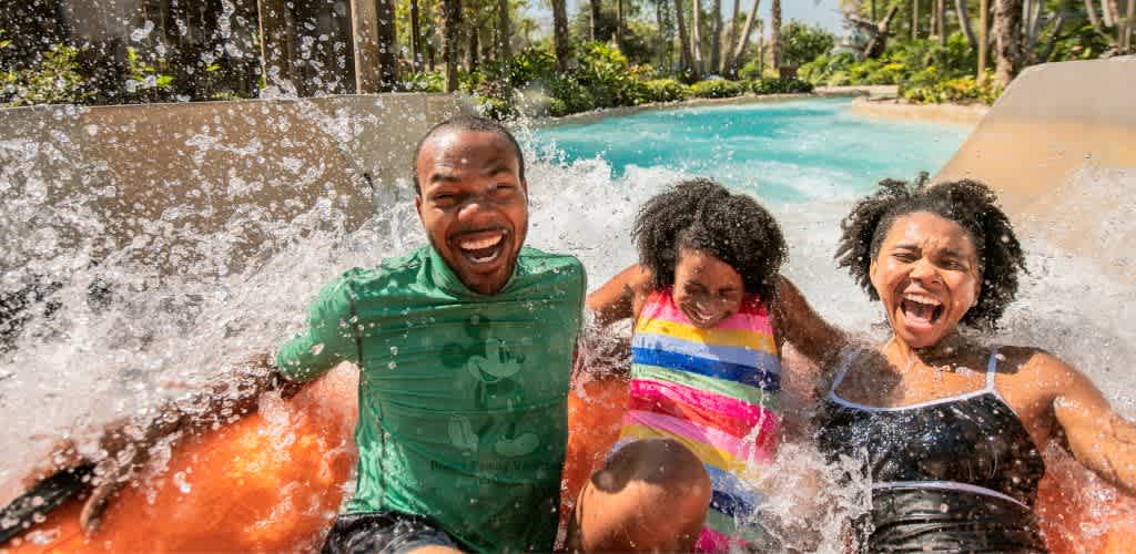 Four people enjoy a water slide outdoors, smiling and splashing as they have fun together on a sunny day.