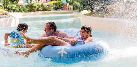 Three children enjoy playing and splashing in a blue inflatable pool outdoors on a sunny day.