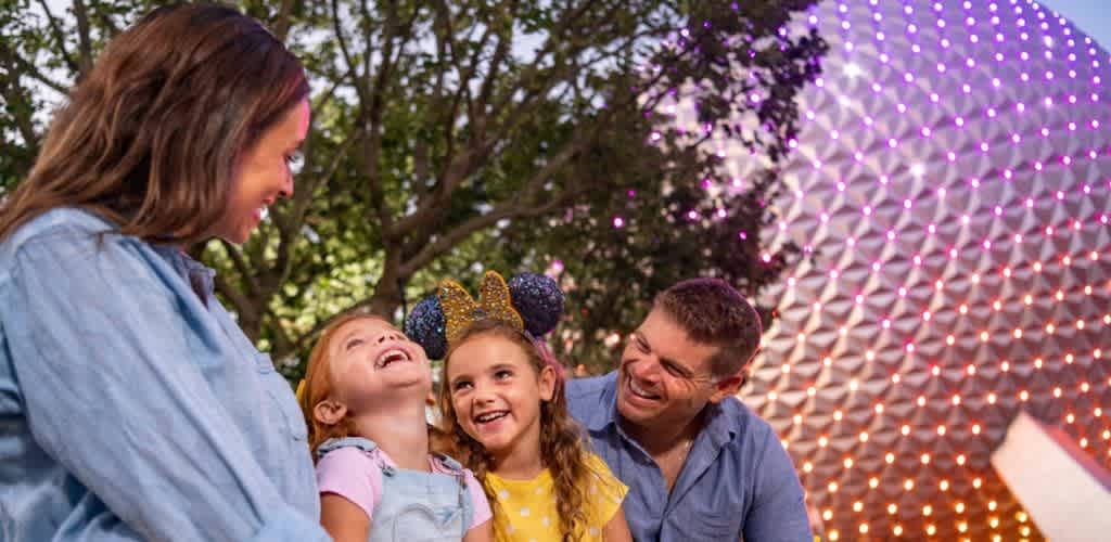 A family enjoying a joyful moment outdoors at nighttime with a large illuminated geodesic dome in the background.
