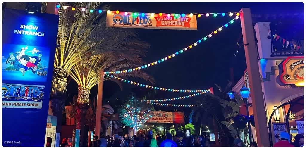 Night scene at Funex amusement park with colorful string lights, palm trees, and crowds enjoying the Grand Pirate Gathering attraction.