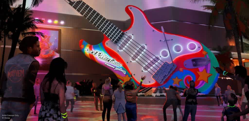 A large colorful guitar-shaped structure decorated with stars and strings, illuminated with vibrant neon lights, and surrounded by people enjoying a lively outdoor event at dusk.